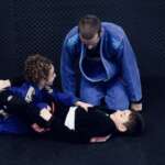 Our bjj coach helping two children with a technique